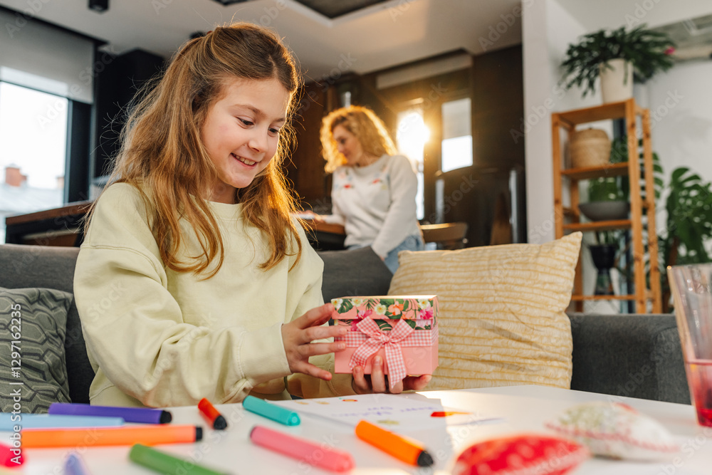 Fototapeta premium Girl holding a gift box for mother's day, preparing a surprise with drawing and colored markers