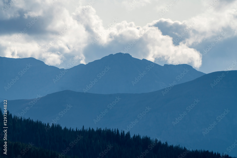 Naklejka premium Majestic mountain peaks loom over a serene forest landscape