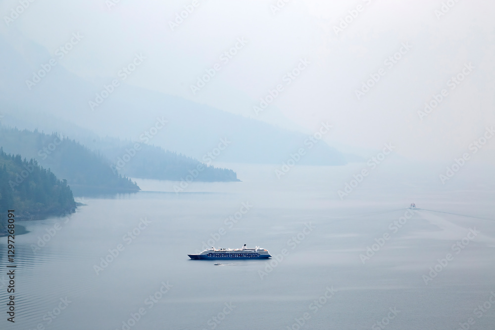 Cruise ship sailing on calm water with misty forest in the background