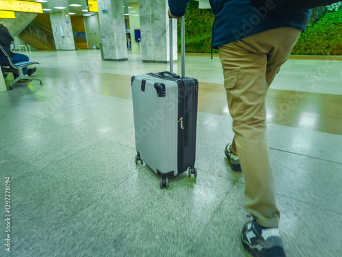 A man pushes a rolling suitcase through a brightly lit airport terminal, wearing casual clothing and a backpack, symbolizing travel and mobility. photo