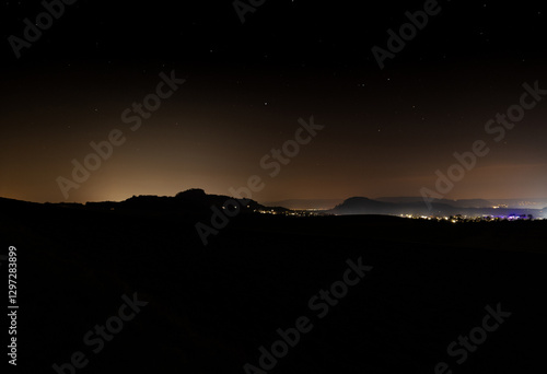 Nighttime landscape showcasing distant mountains and illuminated city skyline under a clear sky
