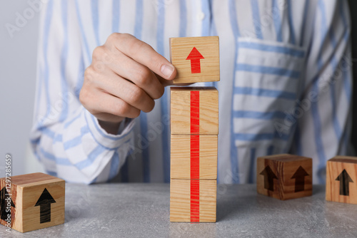 Canvastavla Woman making red arrow of wooden cubes on grey table, closeup