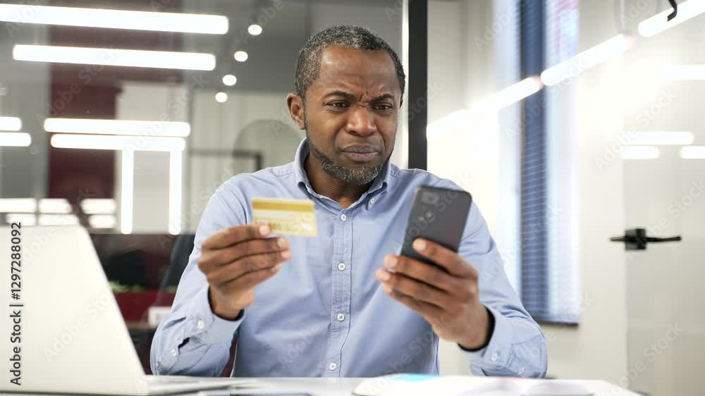 Upset shocked african american businessman checks his credit card on phone sitting in business office. Frustrated male faced fraud, money was stolen from his account. He became a victim of deception Upset shocked african american businessman checks his credit card on phone sitting in business office. Frustrated male faced fraud, money was stolen from his account. He became a victim of deception