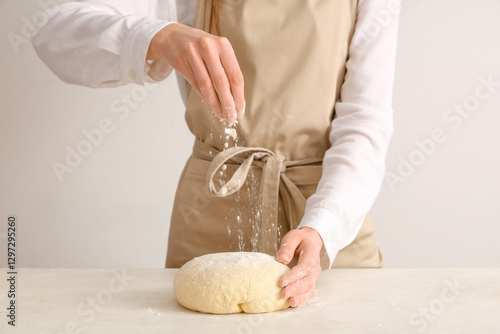 Baker sprinkling flour on d...