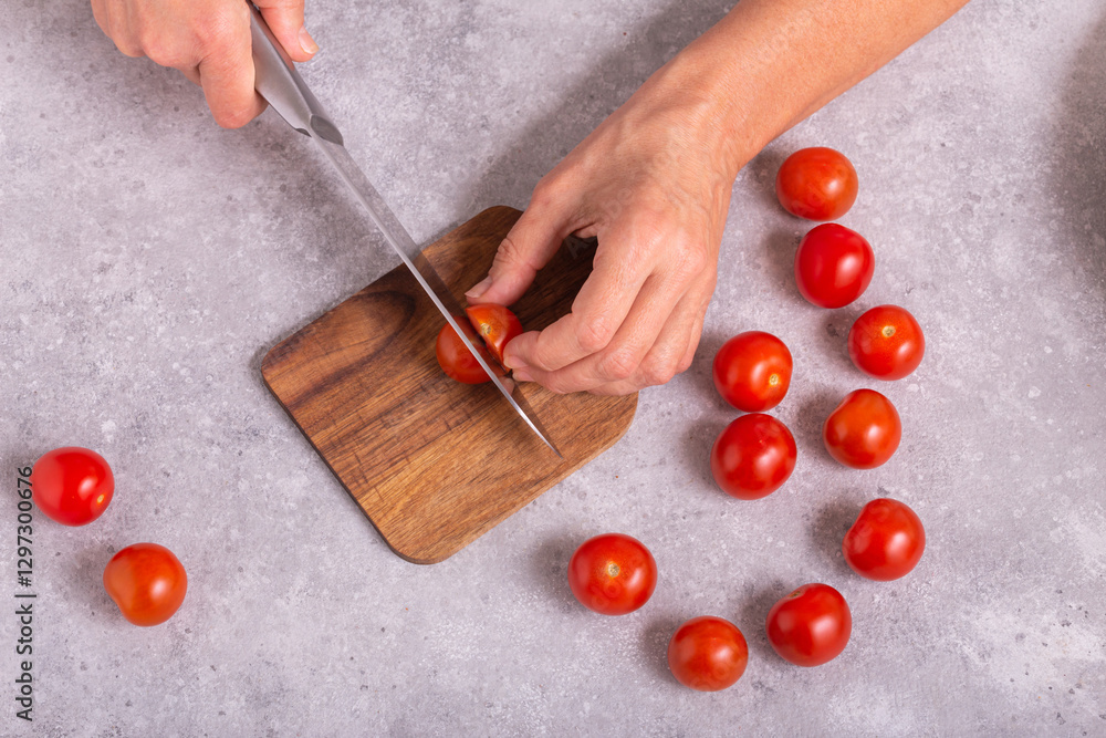 The housewife slicing fresh tomatoes with a large kitchen knife on a wooden chopping board, closeup with selective focus