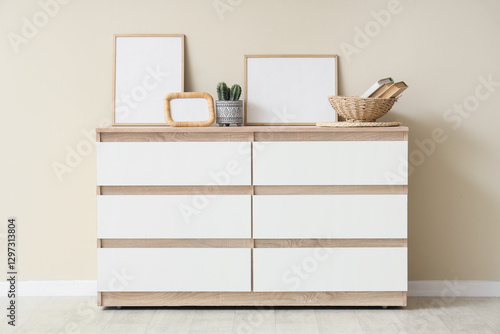 Fotografie Chest of drawers with frames and decor near beige wall in room