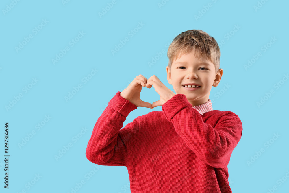 Cute fashionable boy in warm red sweater showing heart shape with hands on blue background Cute fashionable boy in warm red sweater showing heart shape with hands on blue background