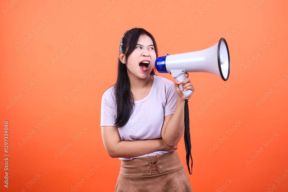 Young woman using a white and blue megaphone yelling on a bright orange background Young woman using a white and blue megaphone yelling on a bright orange background