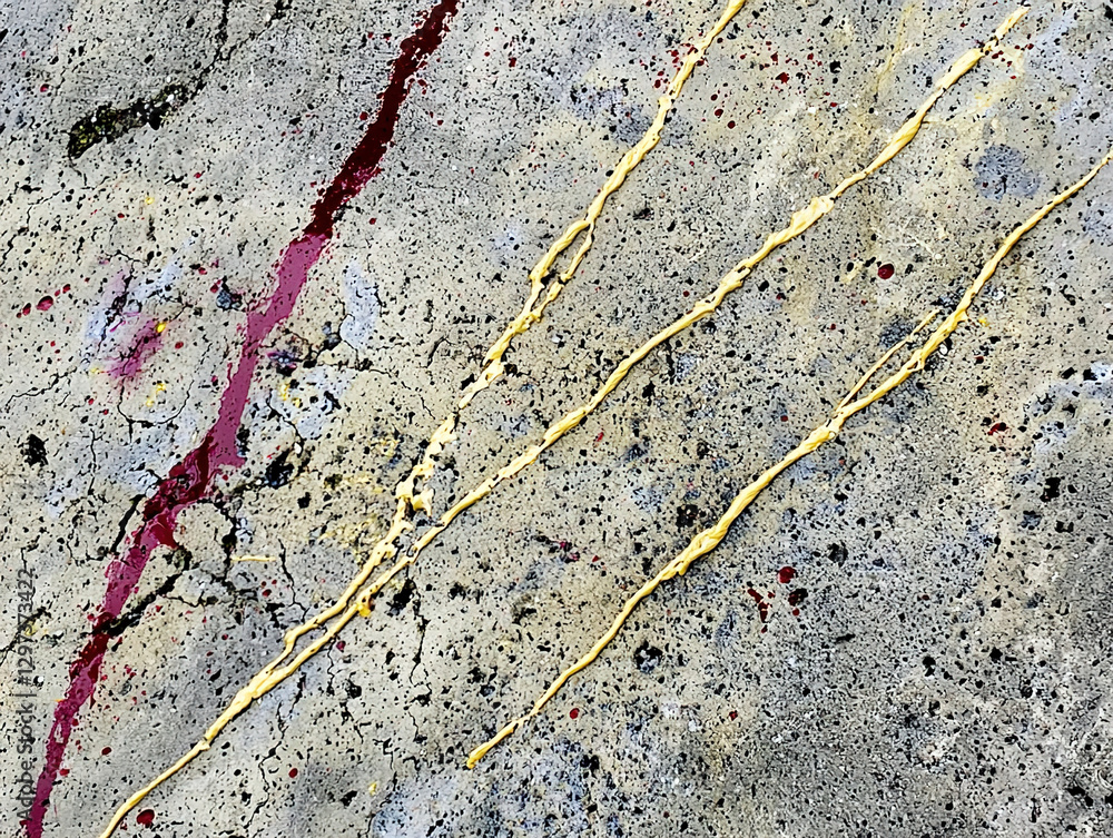 Obraz premium Close-up of a textured concrete surface with gold and red paint splashes and drips.
