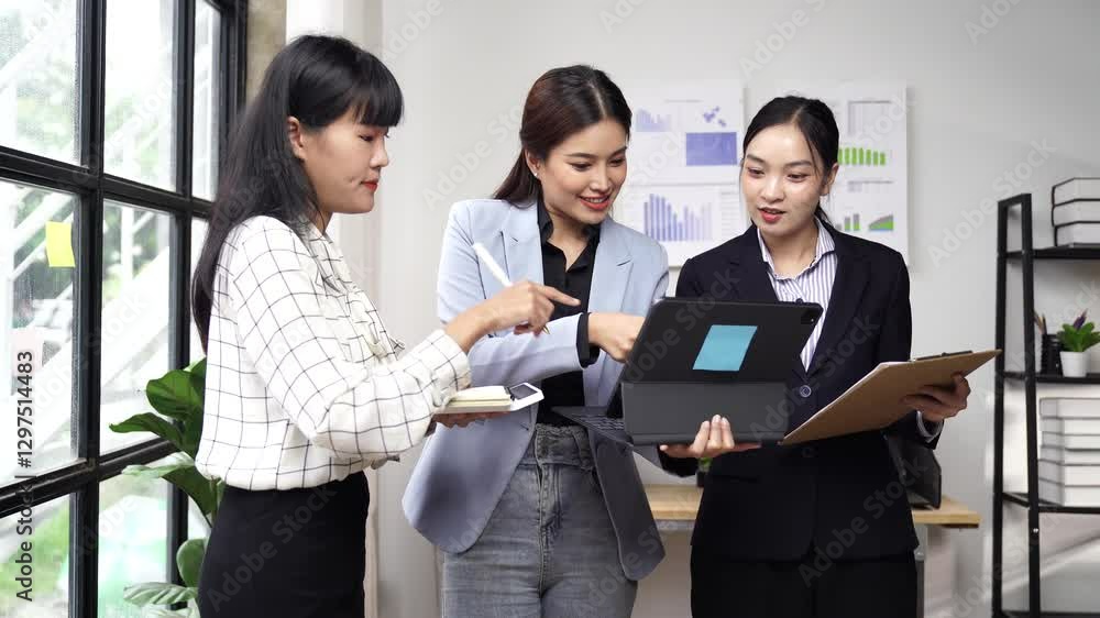 Professional Asian businesswomen collaborating on financial data analysis, reviewing tablet insights in modern office setting while holding clipboard and taking notes Professional Asian businesswomen collaborating on financial data analysis, reviewing tablet insights in modern office setting while holding clipboard and taking notes