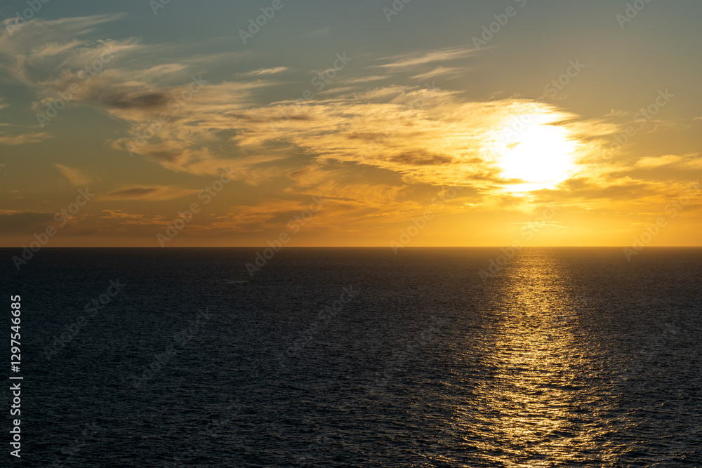 Naklejka premium The sun sets on the horizon over the ocean, with colorful and cloudy skies along the coast of Baja California, Mexico.