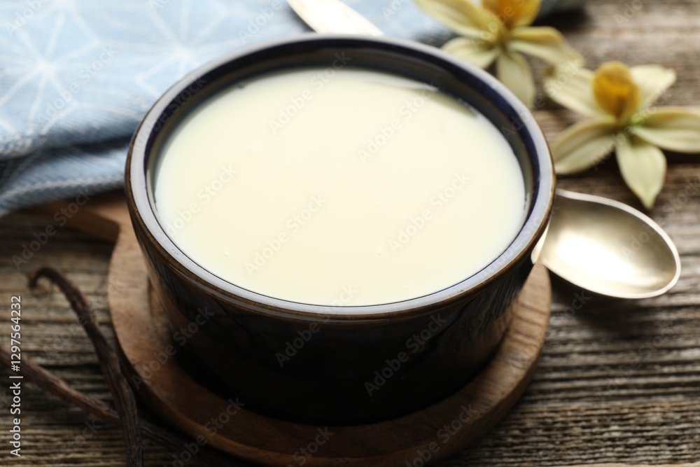 Tasty condensed milk, spoon, vanilla pods and flowers on wooden table, closeup Tasty condensed milk, spoon, vanilla pods and flowers on wooden table, closeup