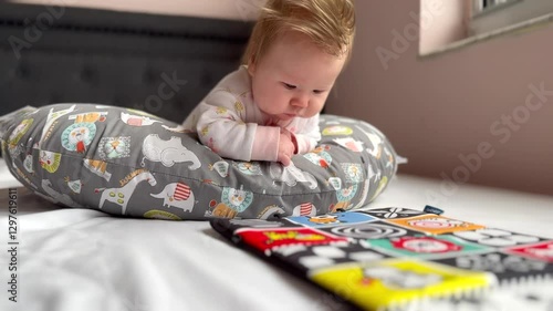 Cute Caucasian newborn baby girl with lots of hair doing tummy time on the pillow and watching high contrast pictures for early learning and baby development. Baby milestone. Pediatrics concept