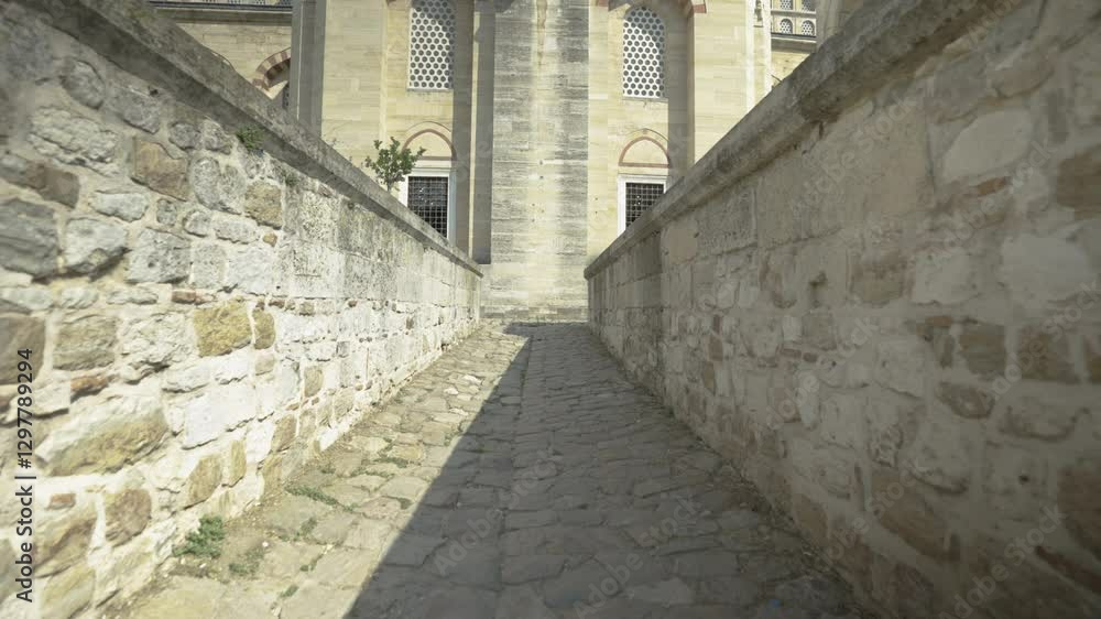 The camera moves backwards in the narrow passageway of the Selimiye Mosque in Edirne, surrounded by stone walls, to reveal the depth of the space and its architectural details.