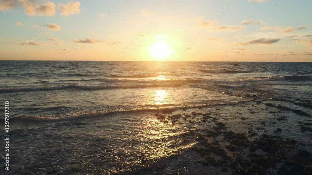 Slow motion - rolling ocean waves to the shore while sunset during tide. Beautiful natural landscape with sandy beach and green plants during low tide. Beautiful wild nature. Sun over horizon. Slow motion - rolling ocean waves to the shore while sunset during tide. Beautiful natural landscape with sandy beach and green plants during low tide. Beautiful wild nature. Sun over horizon.