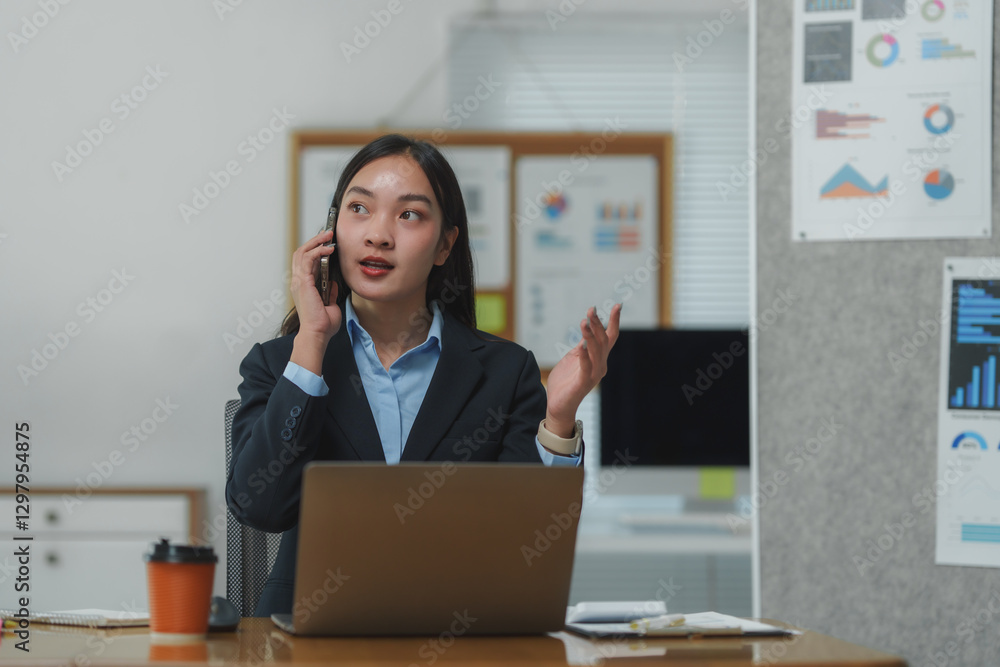 Asian businesswoman talking on phone and gesturing while working on laptop in office Asian businesswoman talking on phone and gesturing while working on laptop in office