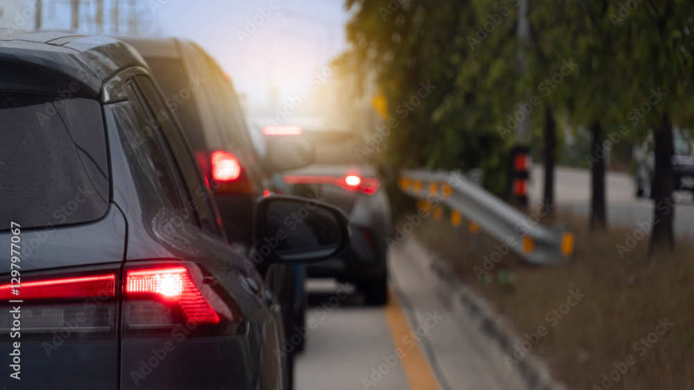 Rear side of cars on the road with turn on brake light. Background is blurred suggesting movement and depth with glimpses of red tail lights and sunlight filtering through trees. Rear side of cars on the road with turn on brake light. Background is blurred suggesting movement and depth with glimpses of red tail lights and sunlight filtering through trees.