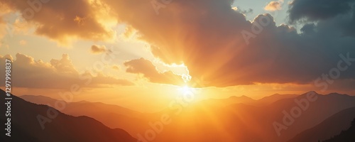 Golden sun rays shine through cloudy sky at sunset over mountain range. Sunlight illuminates mountain peaks silhouette in orange yellow twilight. Majestic alpine dusk landscape, atmospheric scenic