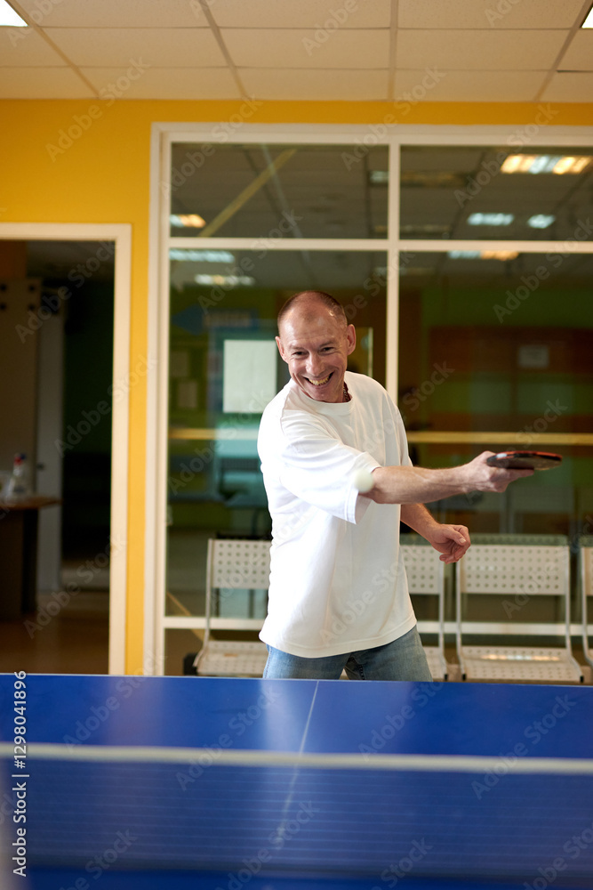 Fototapeta premium A man in a white T-shirt enjoys playing table tennis. Friendly compete in ping pong club