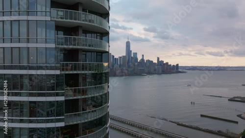 Manhattan skyline revealing One World Trade Center glowing against twilight backdrop, modern residential building in Jersey City in the foreground