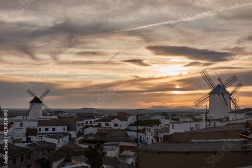 Sunset over the windmills of Campo de Criptana, casting a golden glow on the iconic landscape of Castilla-La Mancha, Spain, famously linked to Don Quixote