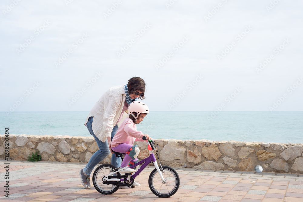 Fototapeta premium Mother teaching her 4 year old daughter to pedal a bicycle.