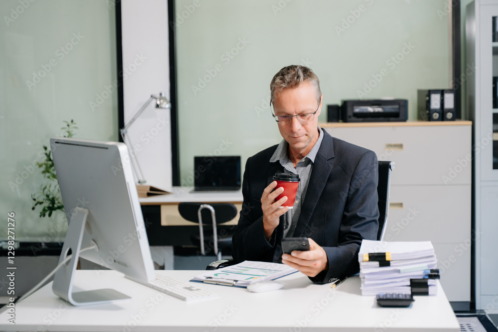 Fototapeta premium Confident businessman in suit, working on laptop and smartphone at office desk. Professional executive