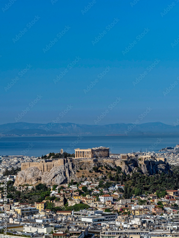 Obraz premium Acropolis of Athens, Greece, with Parthenon in the center. In the background the Aegean Sea and mountains, while in the foreground the city of Athens with a mix of modern and traditional architecture.