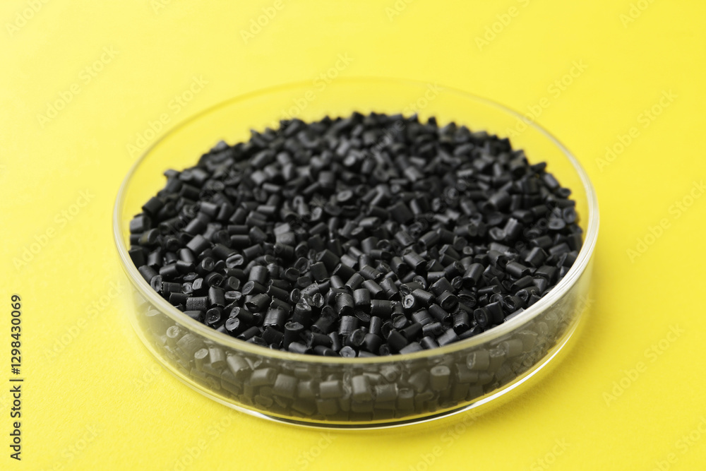 Black plastic granules in petri dish on yellow background, closeup Black plastic granules in petri dish on yellow background, closeup