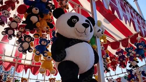 Carnival Prizes: A festive scene at a carnival game, featuring a large panda plush toy and an array of smaller teddy bear prizes, with a red and and white canopy in the background. 