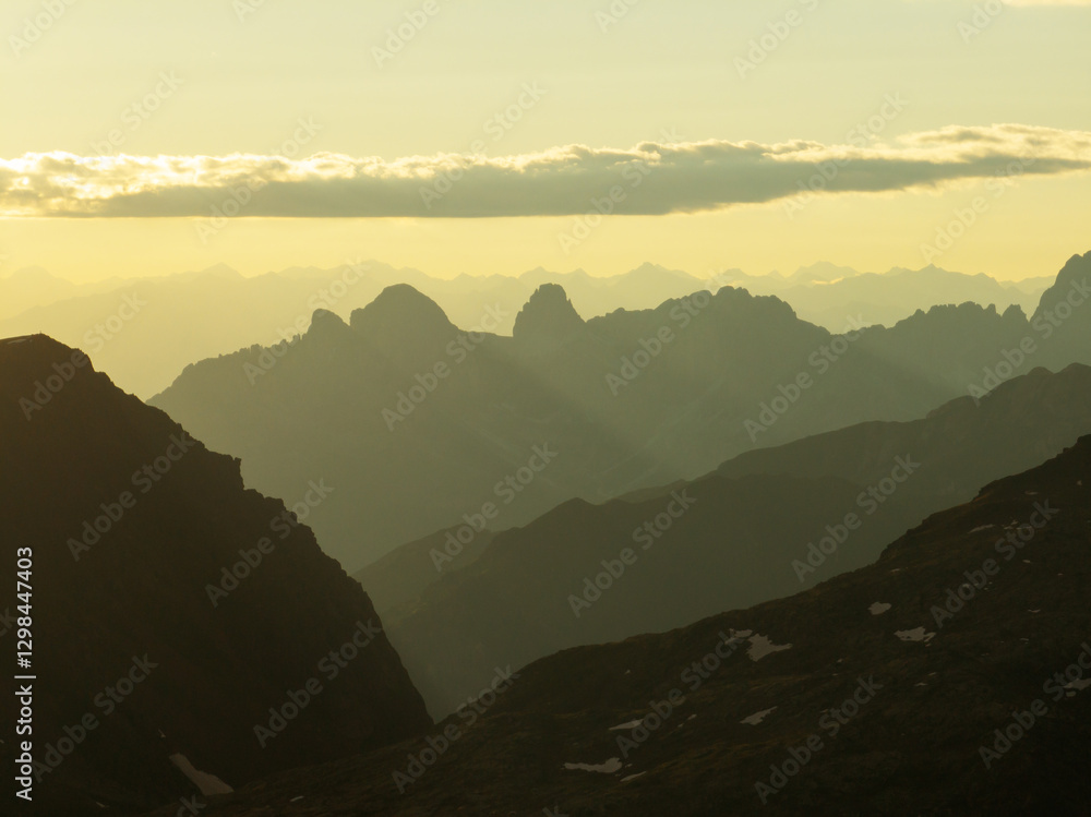 Obraz premium Serene Dolomites at sunset, mountain peaks forming soft layered silhouettes. Warm golden hues fill sky, contrasting misty valleys. Stunning natural scenery attracting hikers, wanderers, landscape love