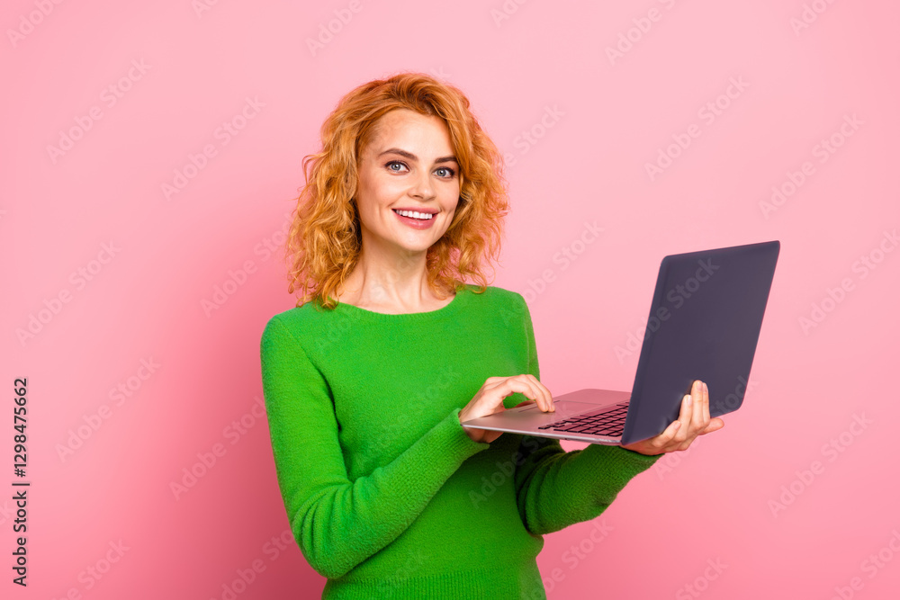 Smiling young woman holding a laptop, standing against a pink background in green attire, conveying a cheerful and fashionable vibe Smiling young woman holding a laptop, standing against a pink background in green attire, conveying a cheerful and fashionable vibe