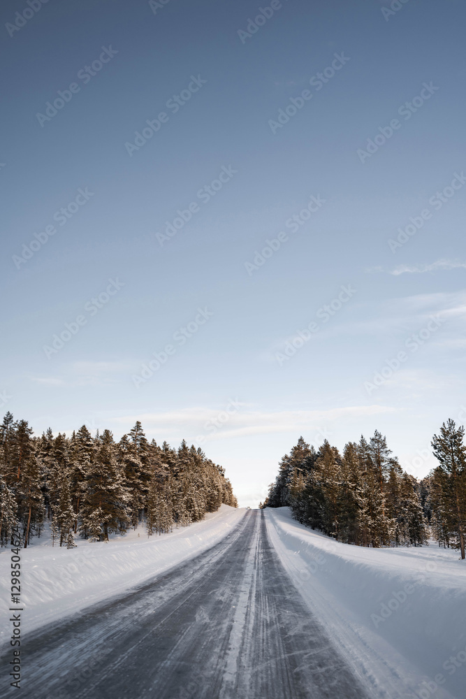 Obraz premium Snow covered road in North Finland on a sunny winter day. Travel Finland landscape background.