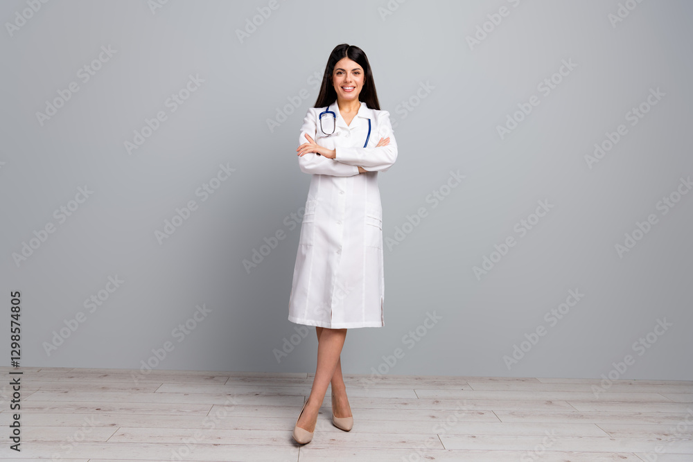 Female doctor with folded arms standing confidently in a white coat on a grey background