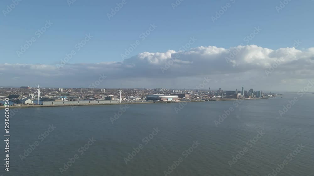 Aerial view of the city of Liverpool from the other side of the river Mersey. Drone moving forwards over the river in direction of the new Everton stadium. Some clouds and blue sky in background. Aerial view of the city of Liverpool from the other side of the river Mersey. Drone moving forwards over the river in direction of the new Everton stadium. Some clouds and blue sky in background.