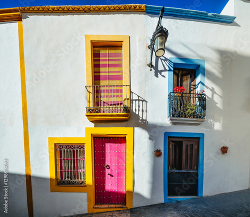 whitewashed facades with coloured windows and doors in a village street decorated with pots and plants. Nijar. Almeria