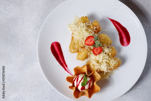Pisang goreng keju (Fried banana with grated cheese) garnished with Pandan leaf served on a white plate above wooden table. Top view close up details 02