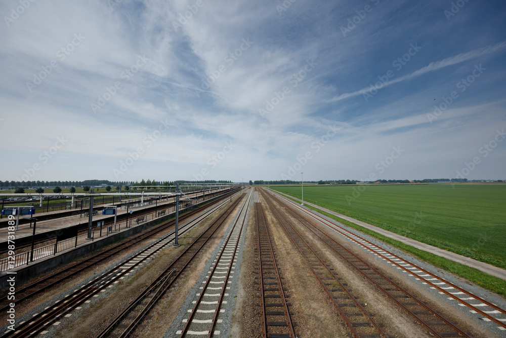 Expansive view of a railway yard surrounded by lush fields under a clear blue sky in the countryside Expansive view of a railway yard surrounded by lush fields under a clear blue sky in the countryside