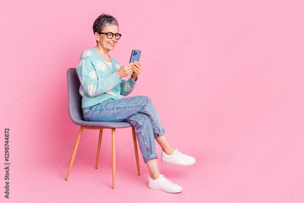 Stylish elderly woman enjoying a casual moment on a pink background, using a smartphone with a smile and wearing a trendy cardigan Stylish elderly woman enjoying a casual moment on a pink background, using a smartphone with a smile and wearing a trendy cardigan