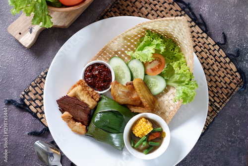 Nasi Timbel Set Meal from  West Java Indonesia, is steamed rice wrap in banana leaf accompanied with chicken, fried tofu,salty fish,tempeh,chilli paste and various raw vegetables. Top view 2