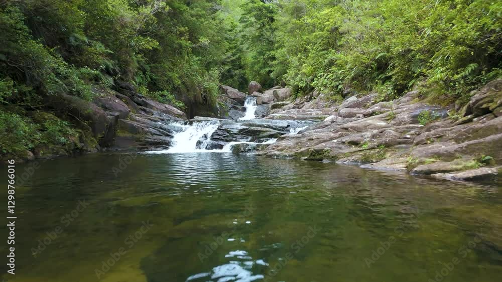 Drone flying low above river stream through rocks, surrounded by lush forest Drone flying low above river stream through rocks, surrounded by lush forest
