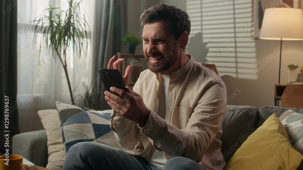 Stressed angry man guy homeowner businessman using mobile phone on sofa at home Caucasian male furious mad annoyed bad message problem browsing smartphone chatting loss failure rejection internet app