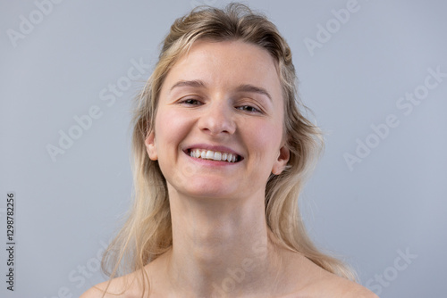 A Bright and Cheerful Young Woman with a Natural Smile and Light Blonde Hair Against a Soft Gray Background, Emphasizing Beauty and Positivity