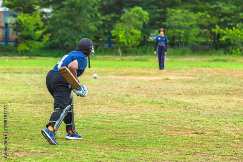 Asian young female cricket player wear protective gear and hitting ball with bat on field. Woman teenager playing cricket in park. Girl with bat and ball on cricket pitch. Sports activity and exercise