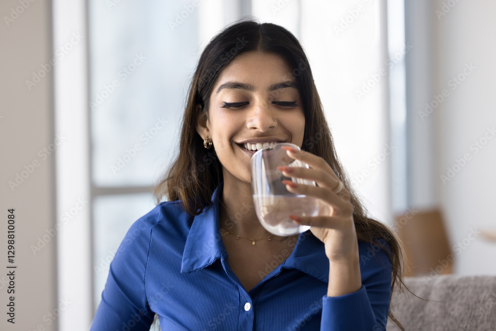 Attractive Indian woman holding glass of still or mineral water seated on sofa at home, making sip, enjoy refreshment, prevents body and skin dehydration, flush out toxins, keeping healthy life habit Attractive Indian woman holding glass of still or mineral water seated on sofa at home, making sip, enjoy refreshment, prevents body and skin dehydration, flush out toxins, keeping healthy life habit