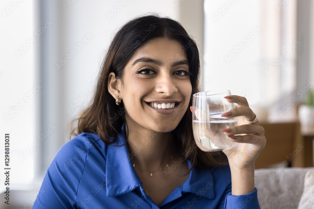 Close up portrait young smiling beautiful Indian woman holding glass of mineral water, looks positive and relaxed, enjoying refreshing drink, promoting hydration and well-being, keep healthy lifestyle Close up portrait young smiling beautiful Indian woman holding glass of mineral water, looks positive and relaxed, enjoying refreshing drink, promoting hydration and well-being, keep healthy lifestyle