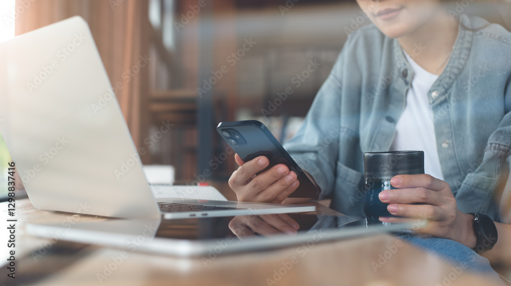 Fototapeta premium Asian business woman drinking coffee and using mobile phone during working on laptop computer at coffee shop. Freelancer online working, using smartphone surfing the internet at cafe
