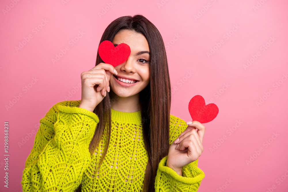 Smiling woman holding red hearts and posing playfully against pink background wearing a vibrant green knitted sweater Smiling woman holding red hearts and posing playfully against pink background wearing a vibrant green knitted sweater