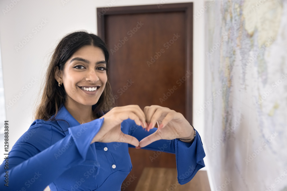 Young Indian woman forms heart shape with her hands while standing near world map, as symbol love of travel, global unity, passion for exploring different cultures, openness to adventures. Wanderlust Young Indian woman forms heart shape with her hands while standing near world map, as symbol love of travel, global unity, passion for exploring different cultures, openness to adventures. Wanderlust