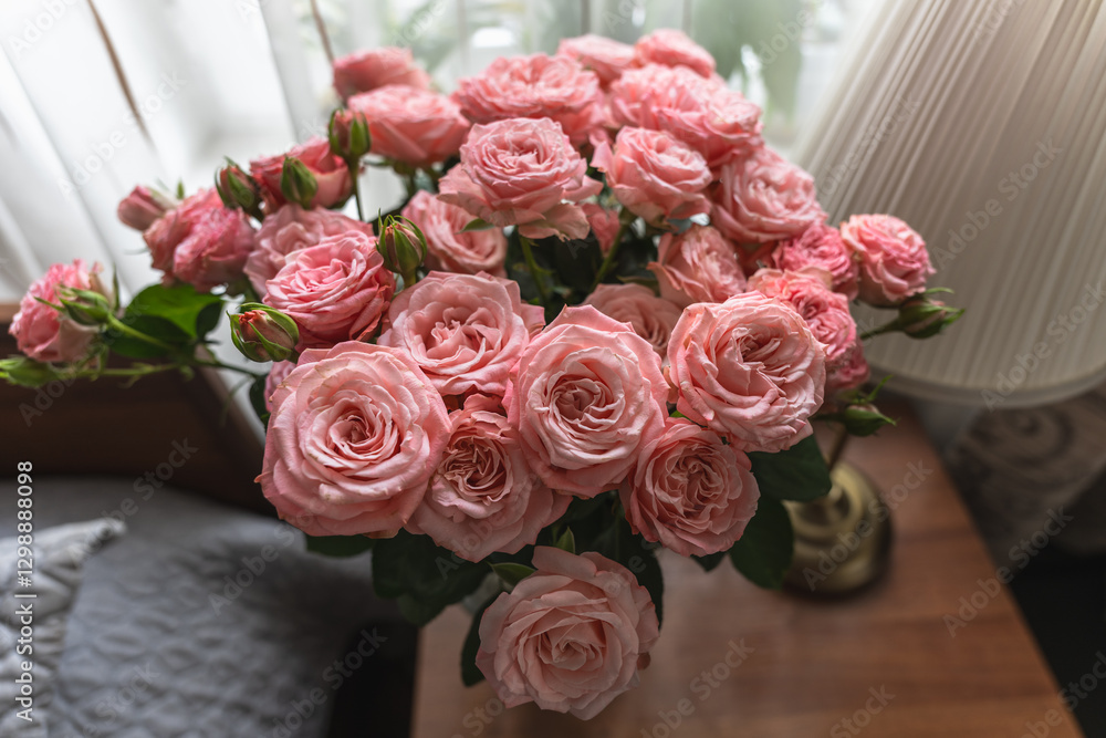 Obraz premium Top view of a large glass vase with a bouquet of pink roses on a bedside table by the window.